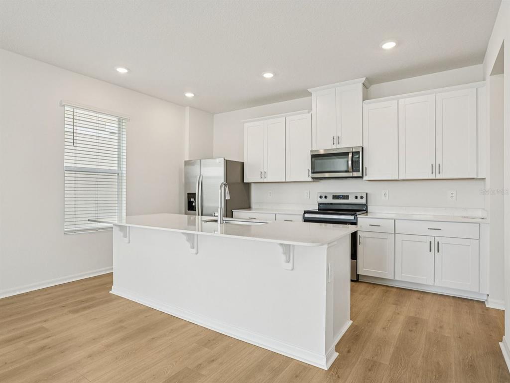 A modern kitchen features white cabinetry, stainless steel appliances, and a large central island — 4688 HOMESTEAD TRAIL, ST CLOUD, FL