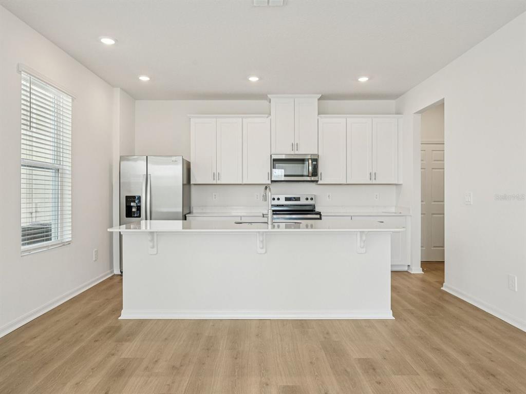 A modern kitchen features white cabinetry, stainless steel appliances, a center island, and wood-look flooring — 4688 HOMESTEAD TRAIL, ST CLOUD, FL