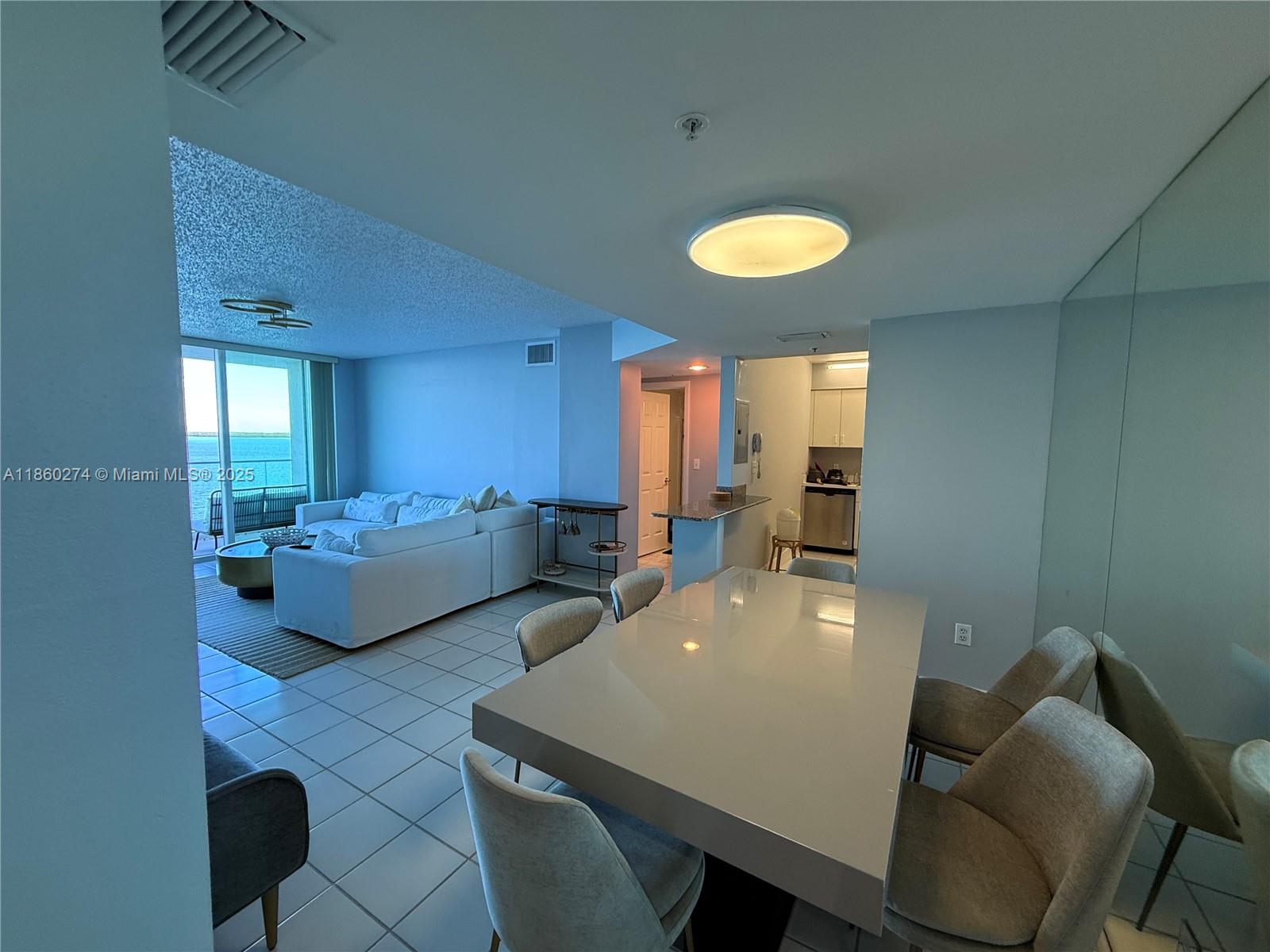 A dining area with a glossy table and chairs opens into a living room with ocean views — 800 Claughton Island Dr # 703, Miami FL 33131, MIAMI, FL