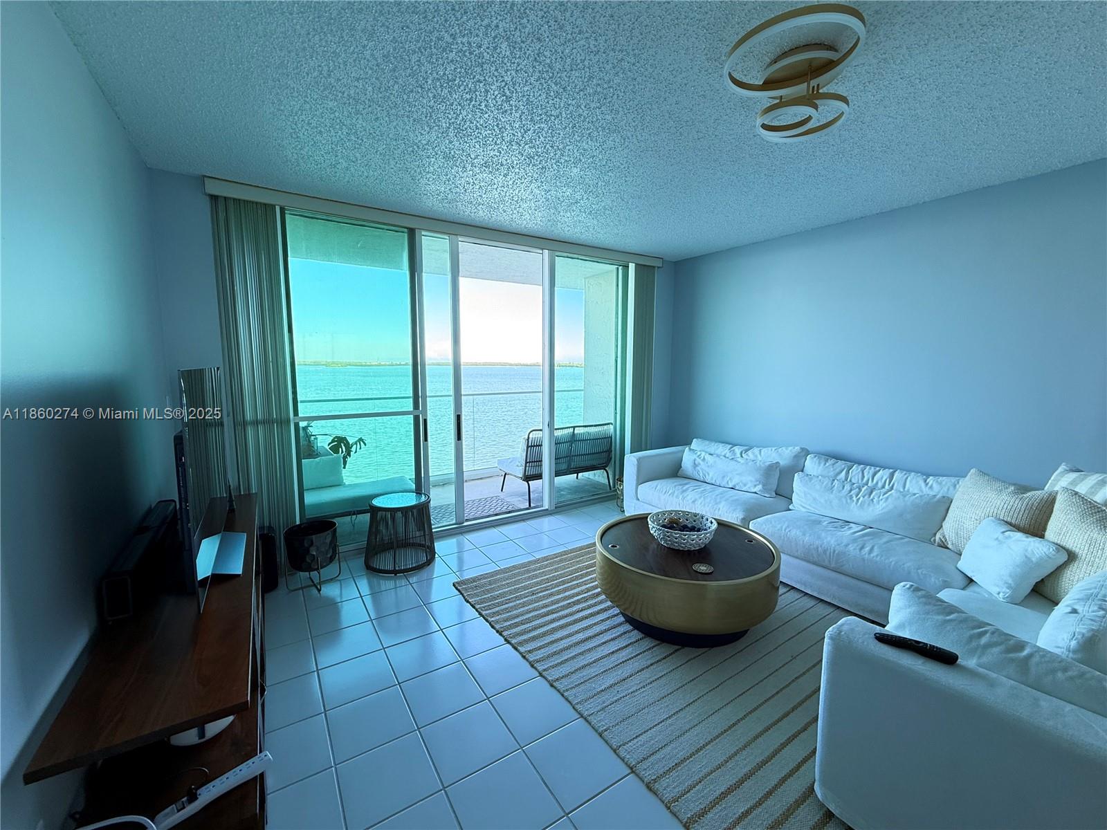 A living room with white tile floors, a white sofa, and a balcony overlooking water — 800 Claughton Island Dr # 703, Miami FL 33131, MIAMI, FL