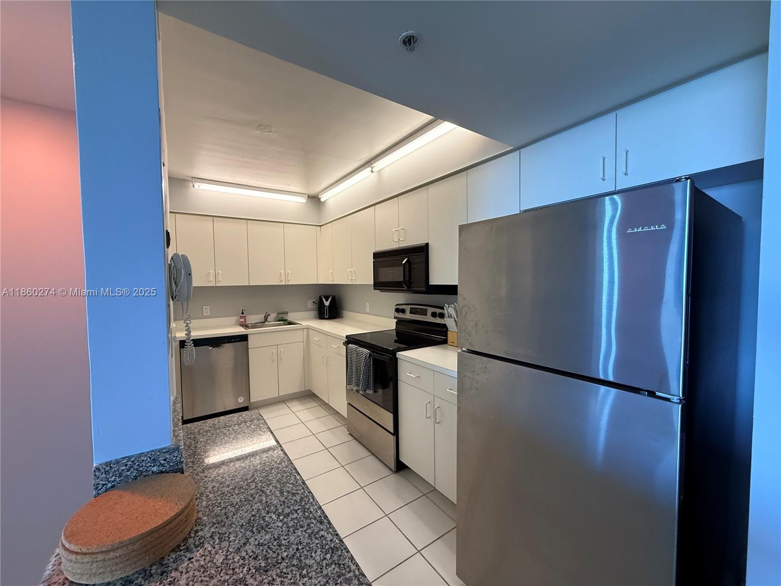 A kitchen features white cabinets, stainless steel appliances, and white tile flooring — 800 Claughton Island Dr # 703, Miami FL 33131, MIAMI, FL