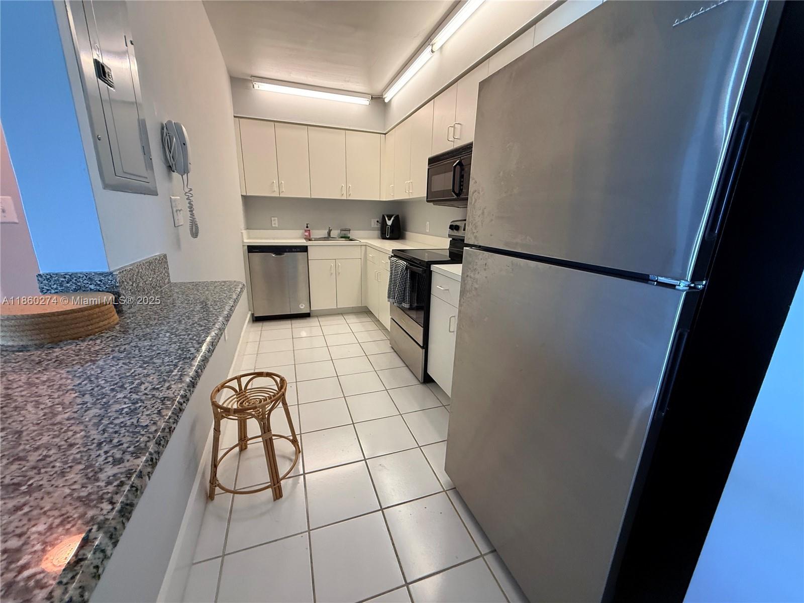 A galley kitchen features white cabinets, stainless steel appliances, and a granite-topped breakfast bar — 800 Claughton Island Dr # 703, Miami FL 33131, MIAMI, FL
