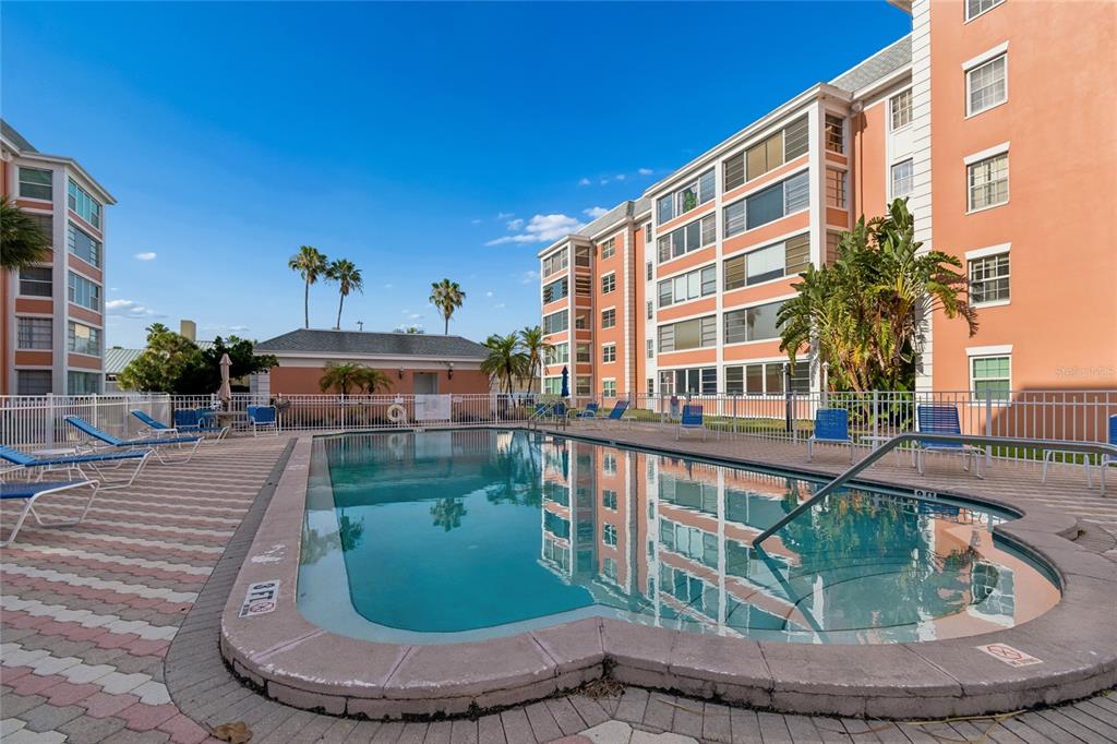 A swimming pool sits in front of multi-story peach-colored apartment buildings under a clear sky — 1900 68TH STREET N UNIT 210, ST PETERSBURG, FL
