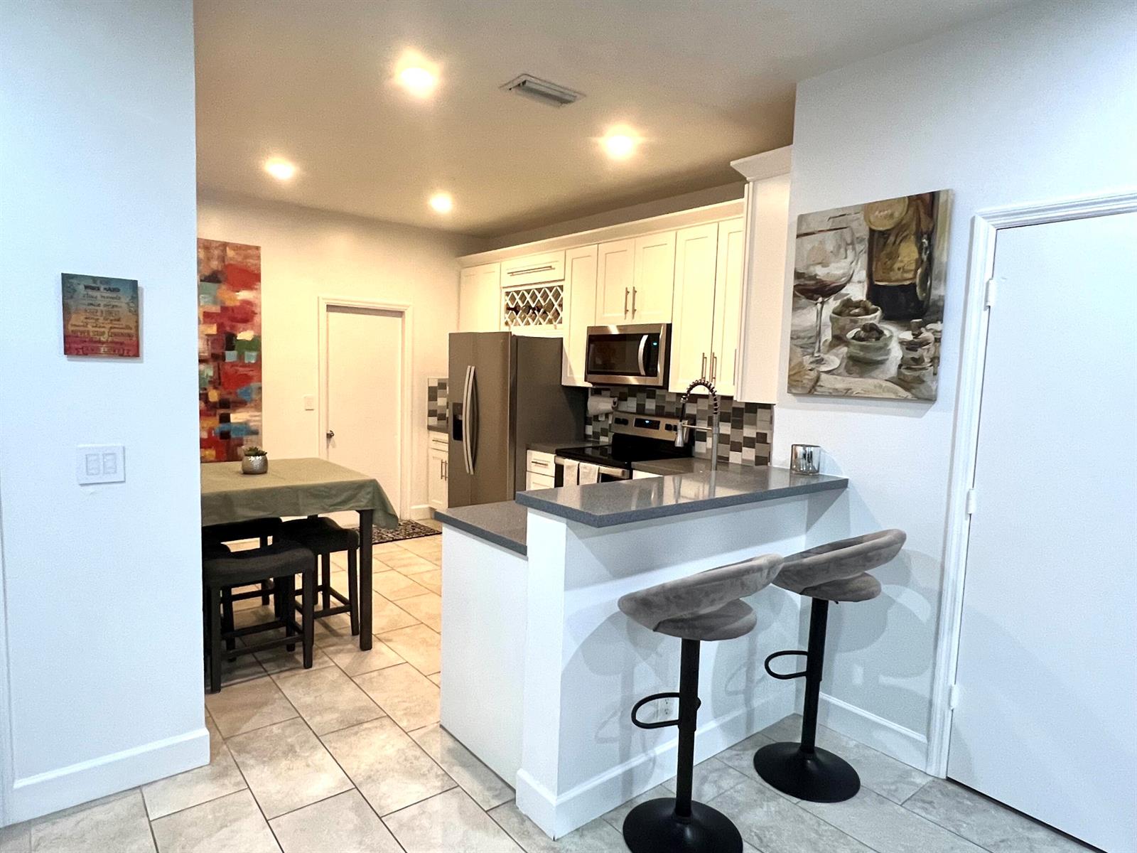 A kitchen features white cabinets, stainless steel appliances, a gray countertop, and two bar stools — 2046 Madeira Drive, Weston FL 33327, WESTON, FL