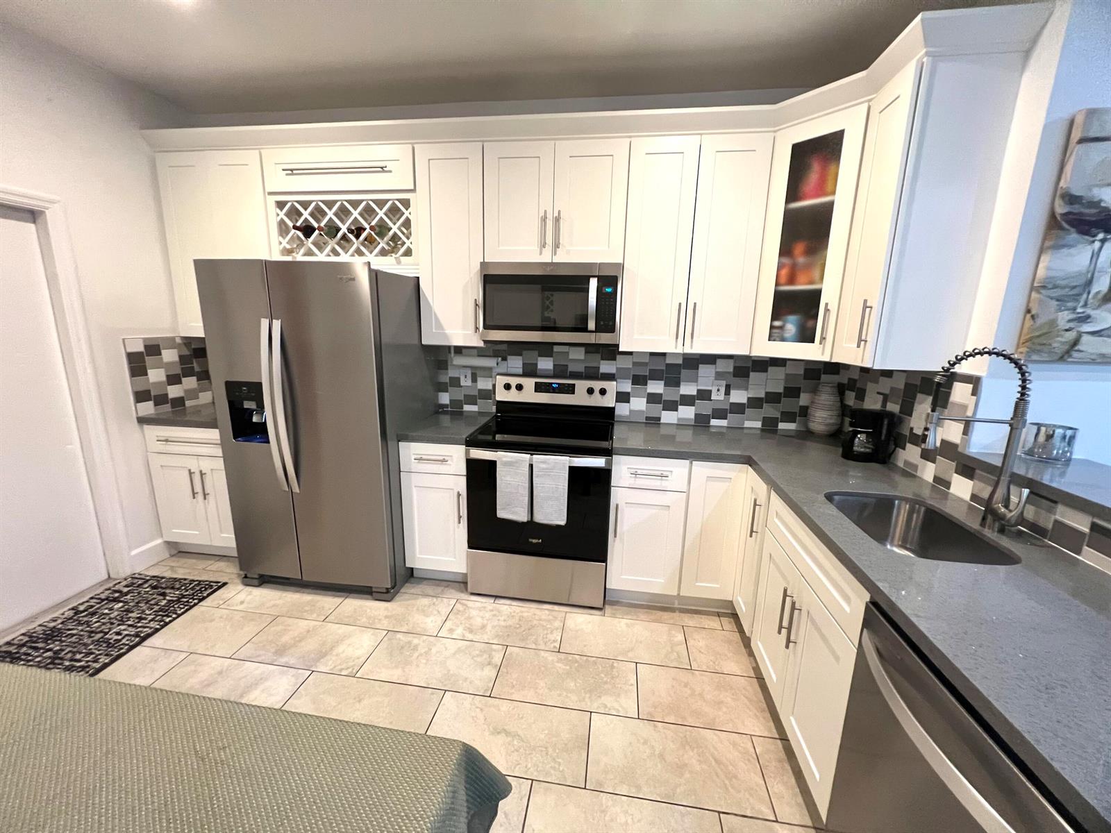 A kitchen features white cabinets, stainless steel appliances, gray countertops, and a tiled backsplash — 2046 Madeira Drive, Weston FL 33327, WESTON, FL