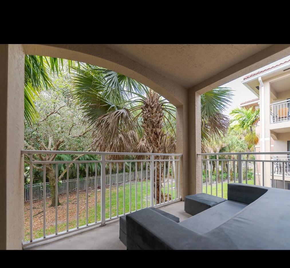 A covered balcony with a grey sofa overlooks a grassy yard and palm trees — 6556 Emerald Dunes Drive # 207, West Palm Beach FL 33411, WEST PALM BEACH, FL