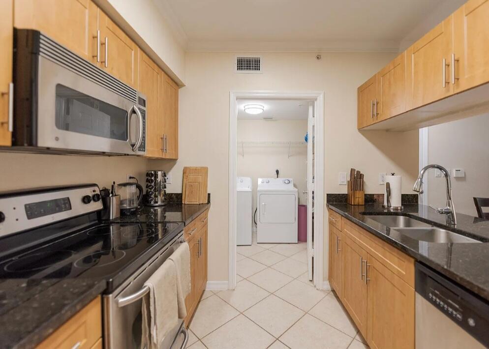A galley kitchen with light wood cabinets, black countertops, and stainless steel appliances — 6556 Emerald Dunes Drive # 207, West Palm Beach FL 33411, WEST PALM BEACH, FL