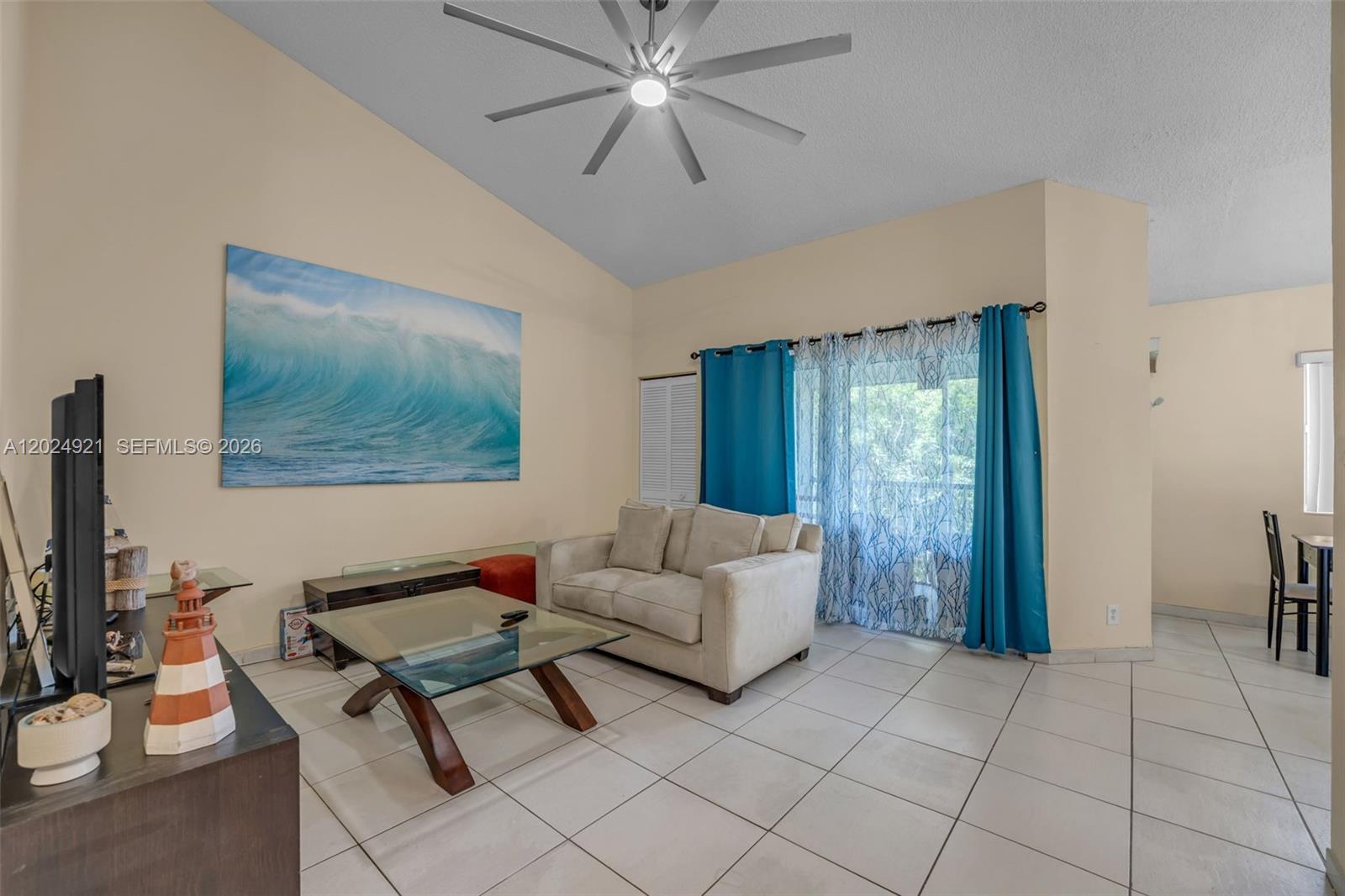 A living room features a vaulted ceiling, tile flooring, a large wave painting, and curtains — 14018 SW 91st Ter # 14018, Miami FL 33186, MIAMI, FL