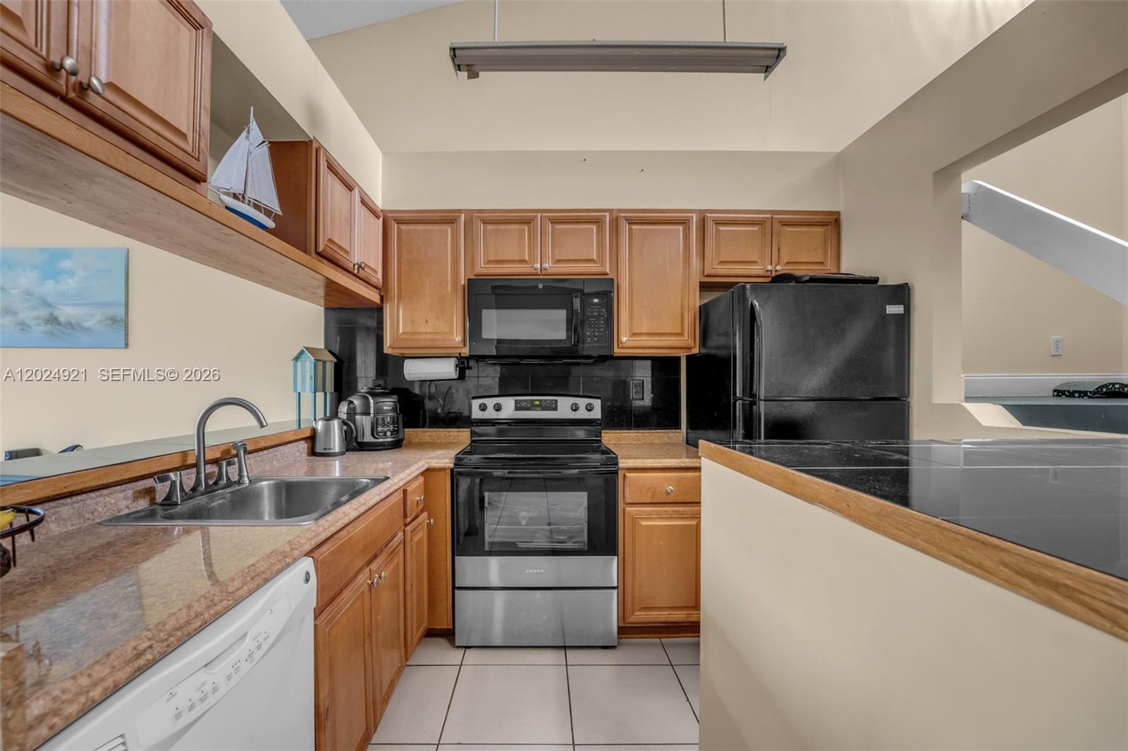 A kitchen features wood cabinets, black appliances, a stainless steel sink, and tile flooring — 14018 SW 91st Ter # 14018, Miami FL 33186, MIAMI, FL