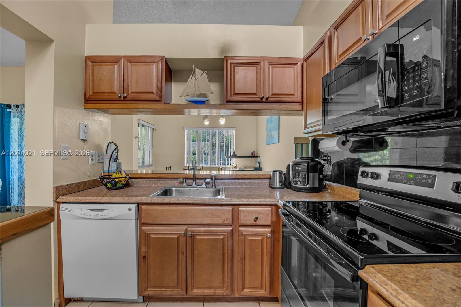 A kitchen features wood cabinets, a white dishwasher, a black stove, and a pass-through window — 14018 SW 91st Ter # 14018, Miami FL 33186, MIAMI, FL