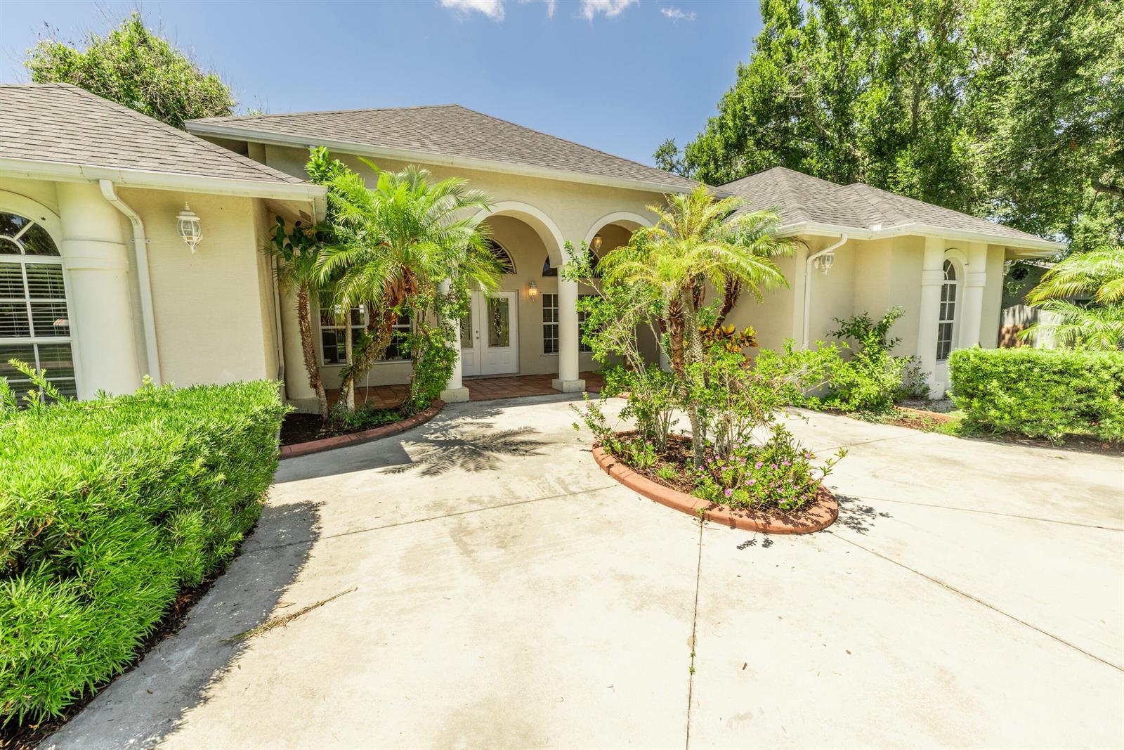 A beige single-story house with a concrete driveway, arched entryway, and palm tree landscaping — 2306 NW 4th Street, Okeechobee FL 34972, OKEECHOBEE, FL