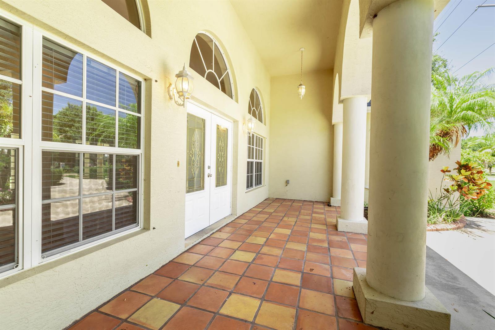 A covered porch features a tiled floor, white columns, and double glass-paneled entry doors — 2306 NW 4th Street, Okeechobee FL 34972, OKEECHOBEE, FL