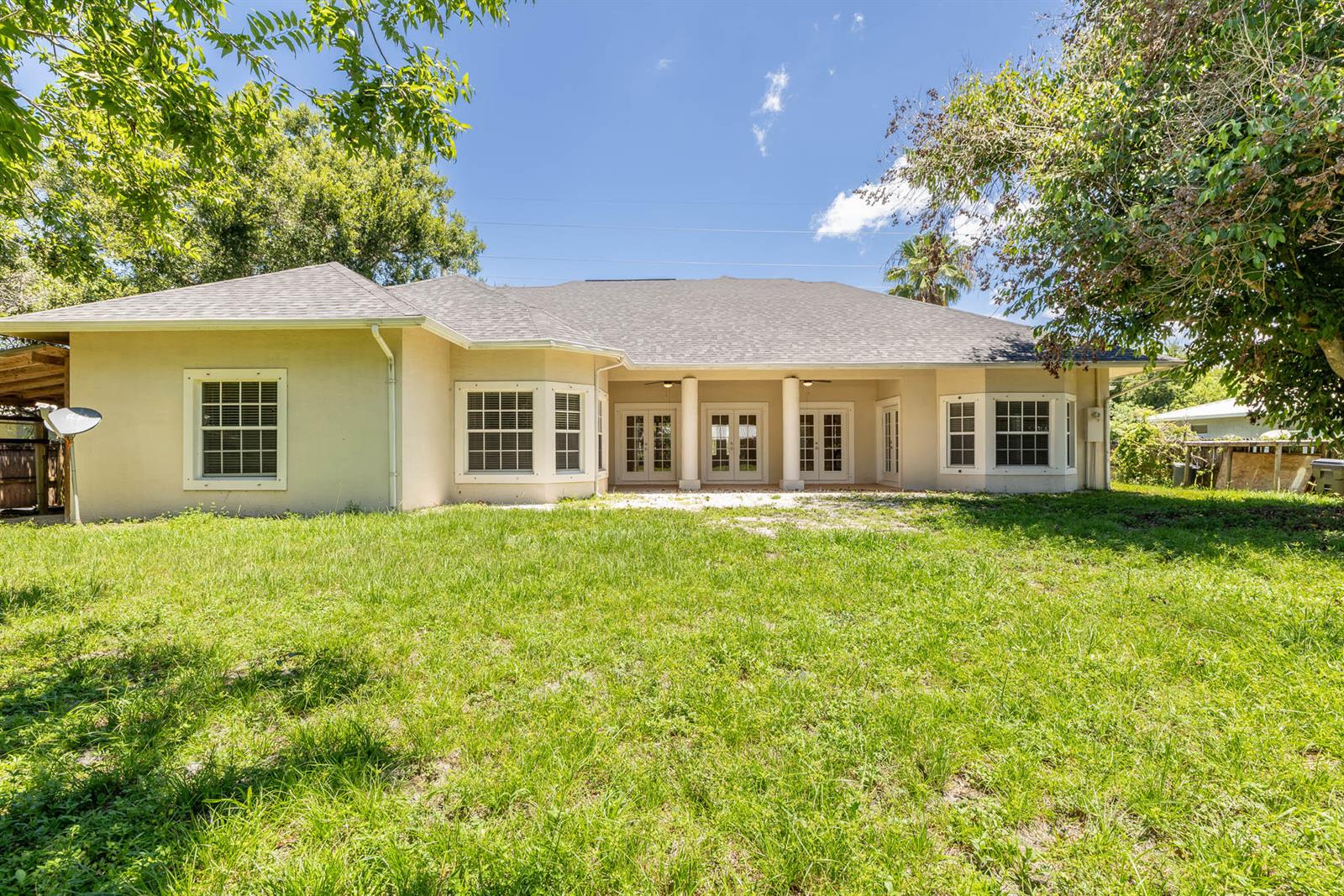 The rear exterior of a single-story house features a covered patio with columns and lawn — 2306 NW 4th Street, Okeechobee FL 34972, OKEECHOBEE, FL