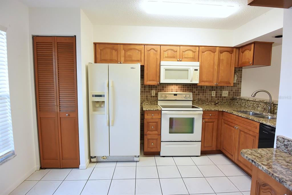 A kitchen features wood cabinets, granite countertops, white appliances, and white tiled flooring — 4908 MYRTLE OAK DRIVE UNIT 12, NEW PORT RICHEY, FL