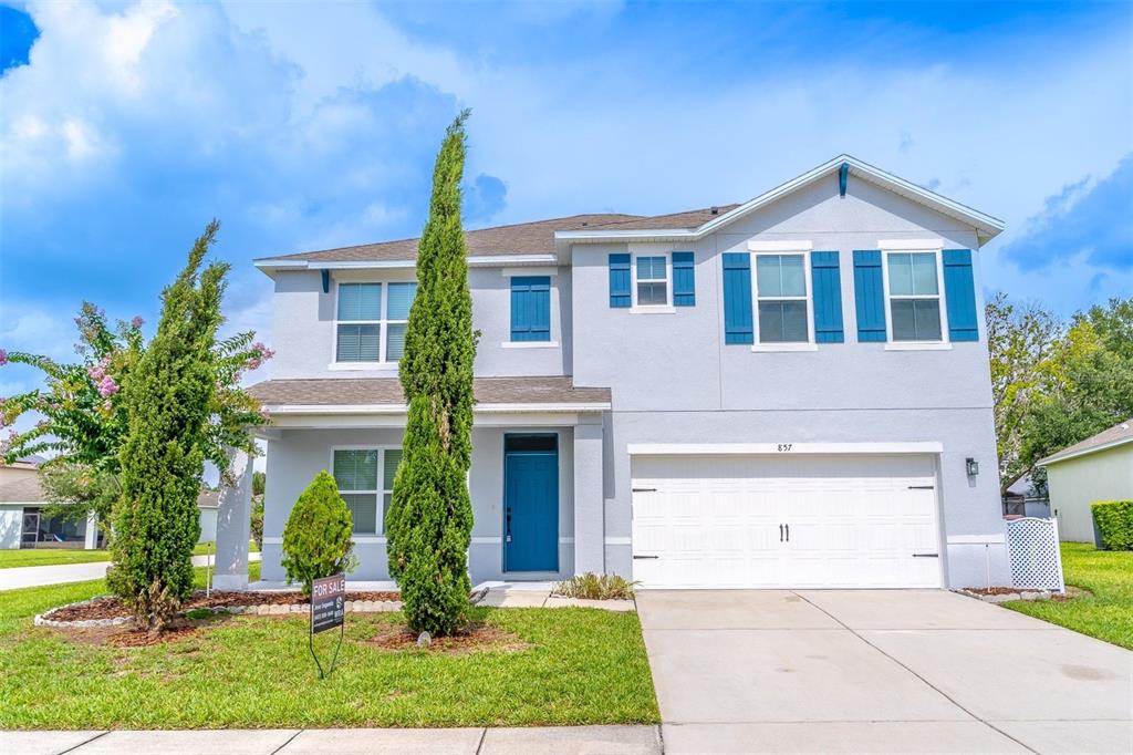 A two-story house with light gray stucco, blue shutters, and a two-car garage — 857 SHEEN CIRCLE, HAINES CITY, FL