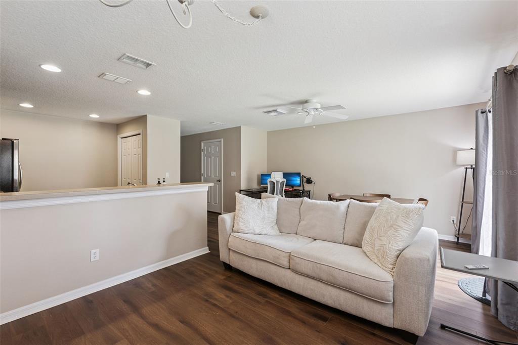A living room with a light-colored sofa, wood-look flooring, and an open kitchen counter — 4246 TRIDENT POINT, OVIEDO, FL