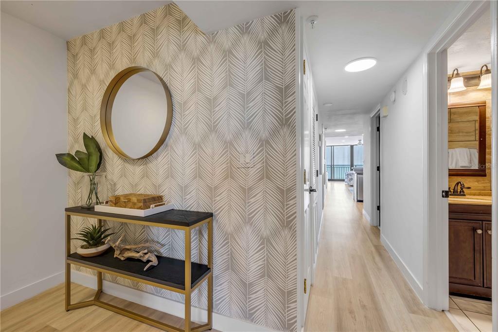 A hallway features a console table, a round mirror, and palm-patterned wallpaper on the wall — 4139 S ATLANTIC AVENUE UNIT B707, NEW SMYRNA BEACH, FL