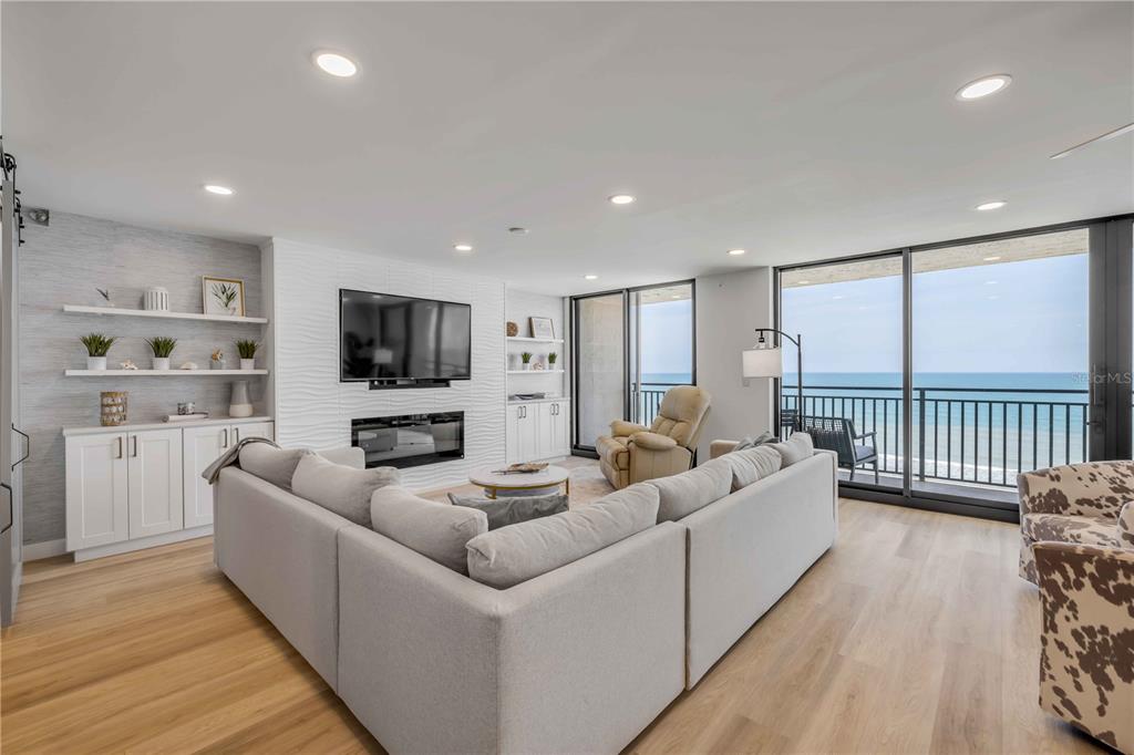A living room features a sectional sofa, a fireplace, built-in shelving, and a balcony view — 4139 S ATLANTIC AVENUE UNIT B707, NEW SMYRNA BEACH, FL