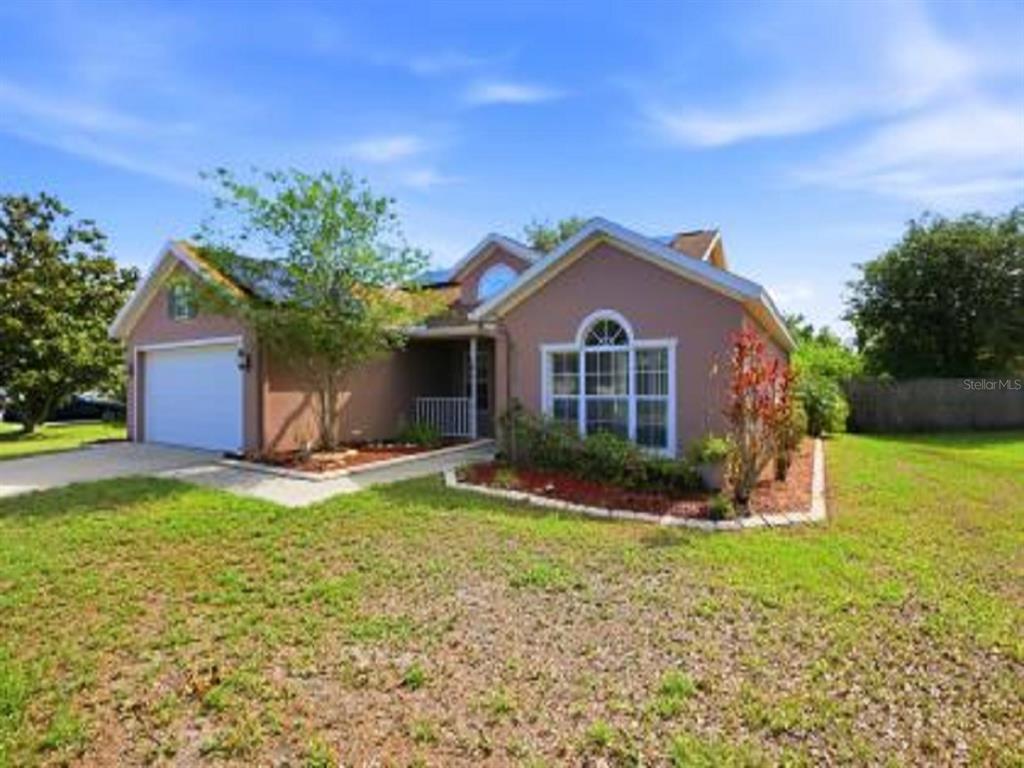 A single-story house with a two-car garage, tan stucco exterior, and a large front lawn — 4199 BANBURY CIRCLE, PARRISH, FL