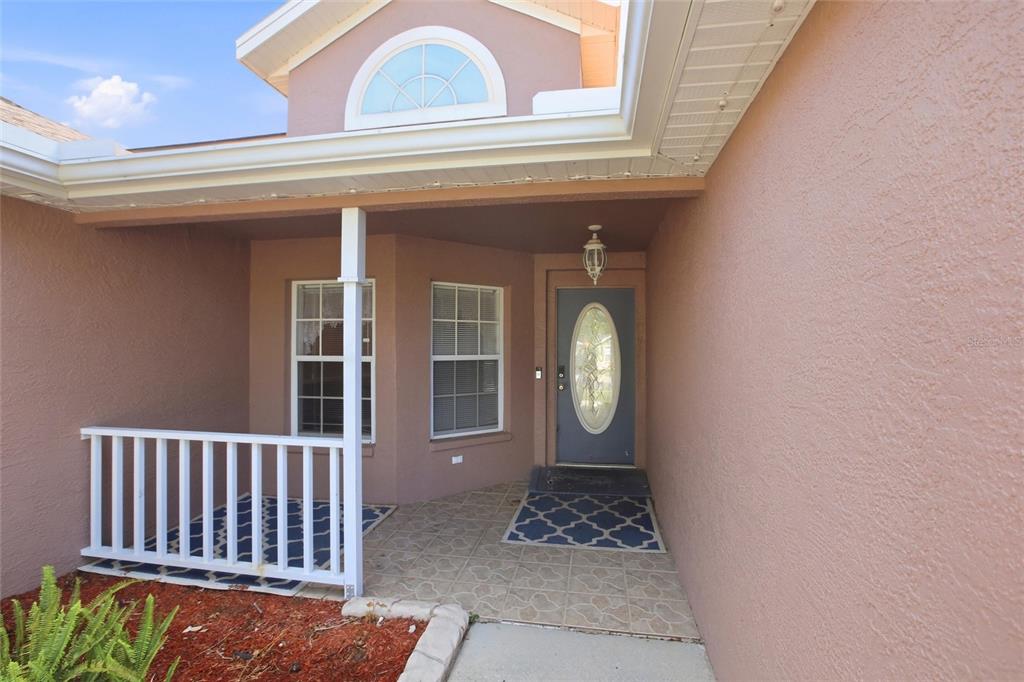 A covered entryway features a blue front door, tiled flooring, and a white wooden railing — 4199 BANBURY CIRCLE, PARRISH, FL