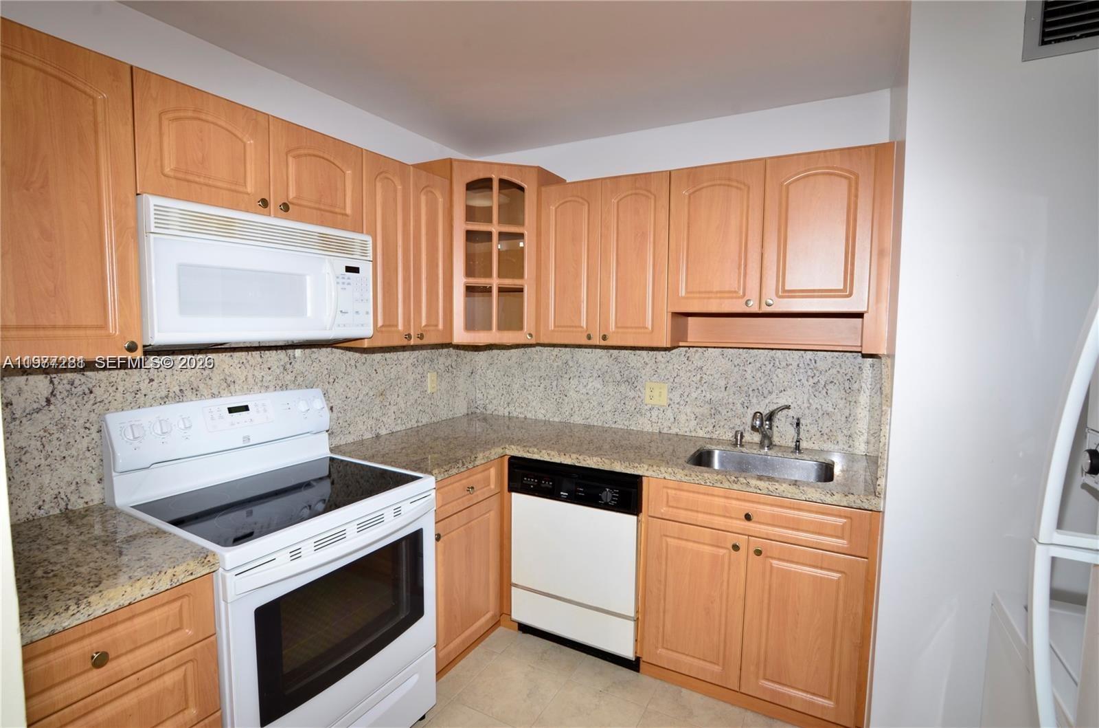 A kitchen features light wood cabinets, granite countertops, and white appliances — 7985 SW 86th St # 432, Miami FL 33143, MIAMI, FL