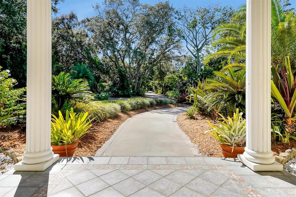 A paved walkway leads through a lush garden, framed by two white columns on a porch — 4209 LAKE LOCKHART DRIVE, ORLANDO, FL
