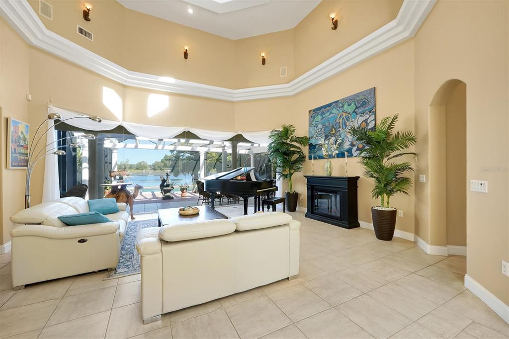 A spacious living room features a grand piano, white sofas, and a view of water — 4209 LAKE LOCKHART DRIVE, ORLANDO, FL