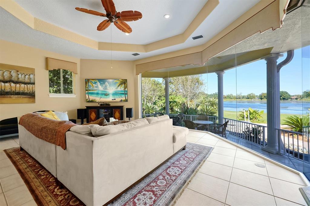 A living room with a large sectional sofa, tile floors, and floor-to-ceiling windows overlooking water — 4209 LAKE LOCKHART DRIVE, ORLANDO, FL