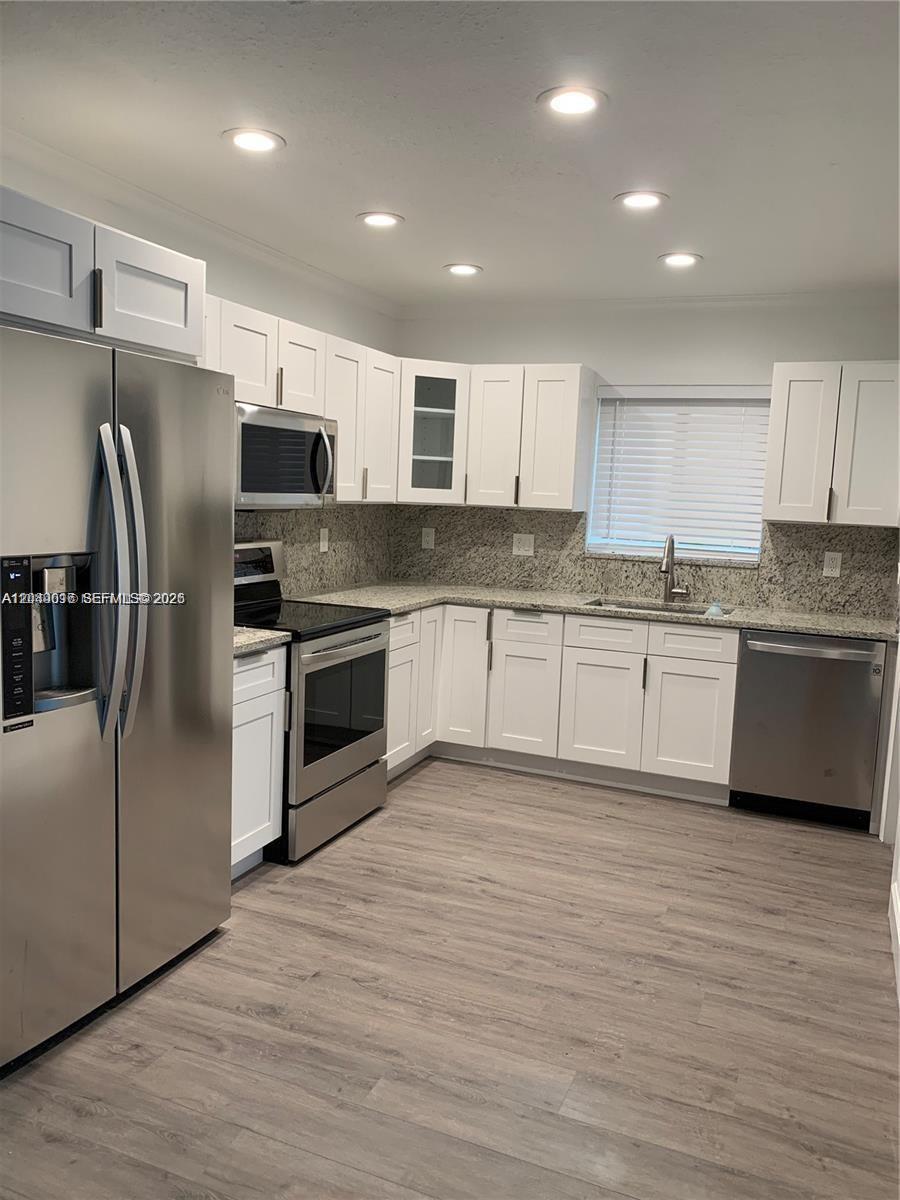 A kitchen features white cabinets, stainless steel appliances, granite countertops, and light wood-look flooring — 28 SE 7th St, Dania Beach FL 33004, DANIA BEACH, FL