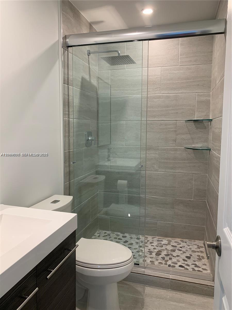 A modern bathroom features a glass-enclosed shower with a pebble floor and gray tile walls — 28 SE 7th St, Dania Beach FL 33004, DANIA BEACH, FL