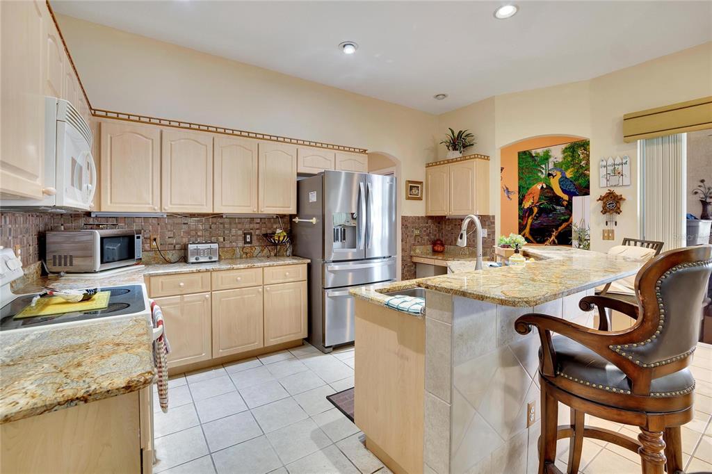A kitchen features light wood cabinets, granite countertops, stainless steel appliances, and a breakfast bar — 813 INNERGARY PLACE, VALRICO, FL