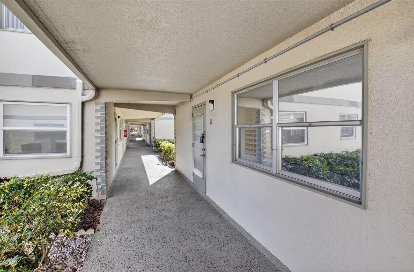 An outdoor walkway leads past a unit door and window in a multi-story apartment complex — 61 Brittany B # 61, Delray Beach FL 33446, DELRAY BEACH, FL