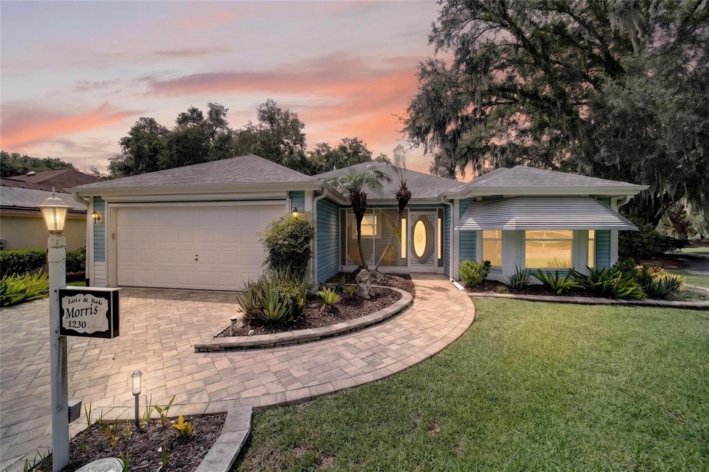 A single-story blue house with a paved walkway and a two-car garage at sunset — 1230 DESILVA STREET, THE VILLAGES, FL