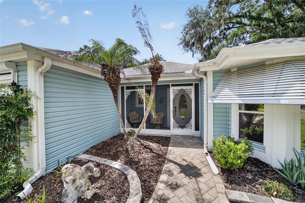 A light blue house exterior features a paved walkway leading to a screened front entryway — 1230 DESILVA STREET, THE VILLAGES, FL