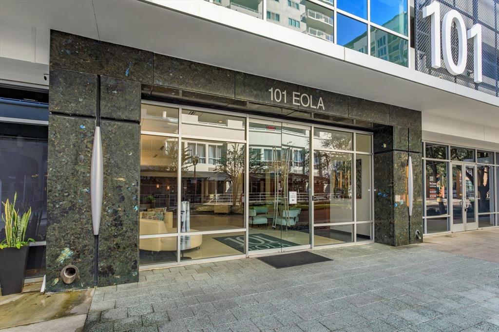 The exterior entrance of a modern building features glass doors, dark stone cladding, and signage — 101 S EOLA DRIVE UNIT 1021, ORLANDO, FL