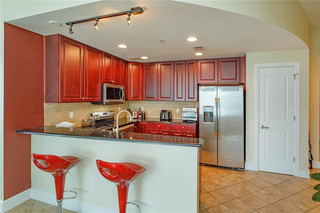 A kitchen features cherry wood cabinets, black granite countertops, stainless steel appliances, and red barstools — 101 S EOLA DRIVE UNIT 1021, ORLANDO, FL