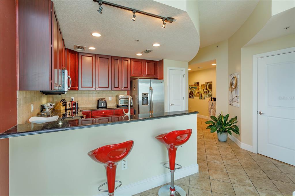 A kitchen with dark wood cabinets, granite countertops, and two red bar stools — 101 S EOLA DRIVE UNIT 1021, ORLANDO, FL
