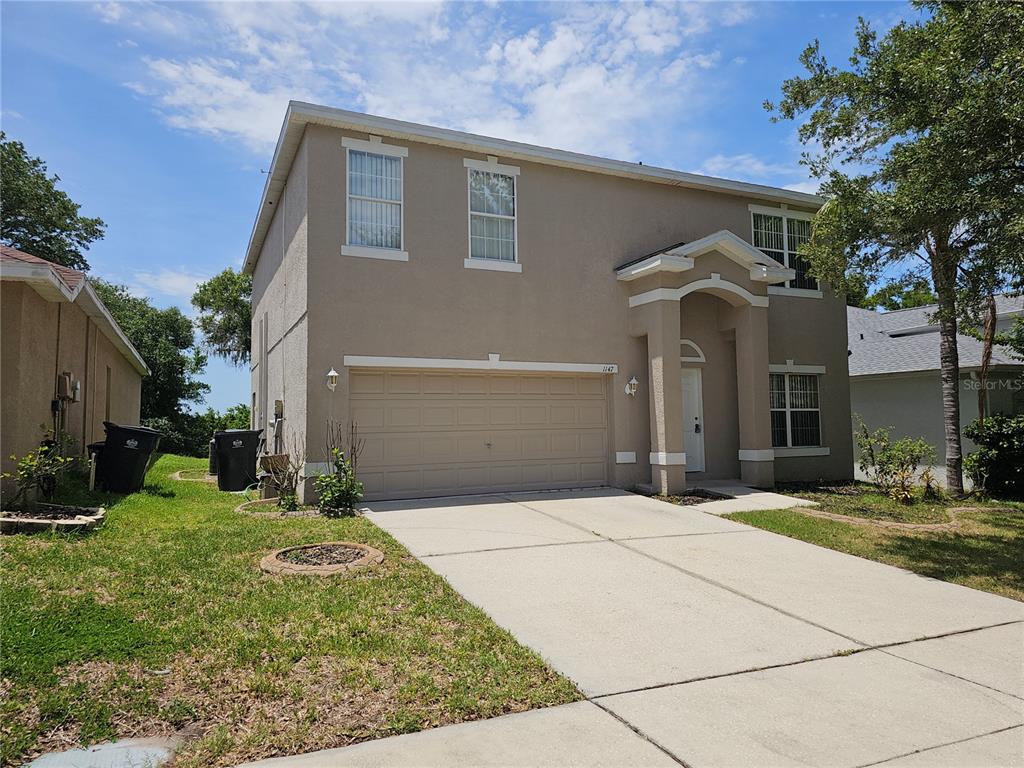 A two-story tan stucco house features a two-car garage and a covered front entryway — 1147 EMERALD HILL WAY, VALRICO, FL