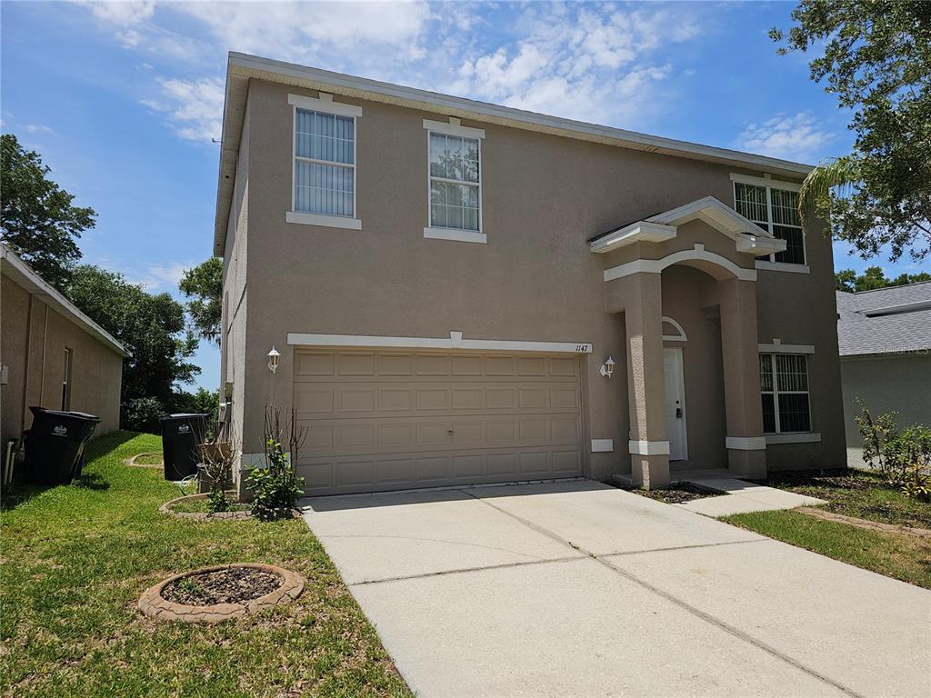 A two-story suburban house with a beige stucco exterior, a two-car garage, and a driveway — 1147 EMERALD HILL WAY, VALRICO, FL