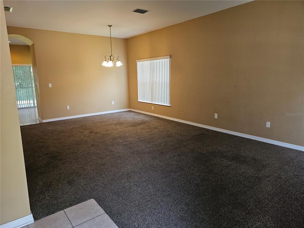 An empty room with tan walls, dark carpeting, a chandelier, and vertical window blinds — 1147 EMERALD HILL WAY, VALRICO, FL