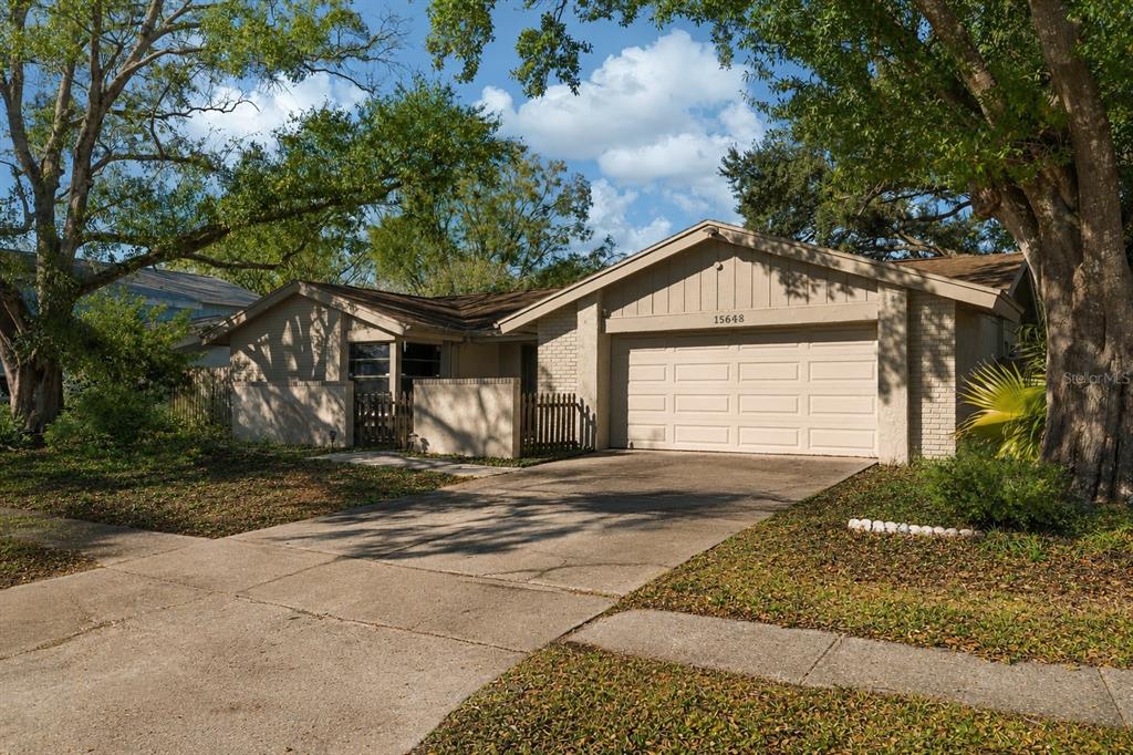 A single-story house with a beige exterior, a two-car garage, and a concrete driveway — 15648 BEAR CREEK DRIVE, TAMPA, FL