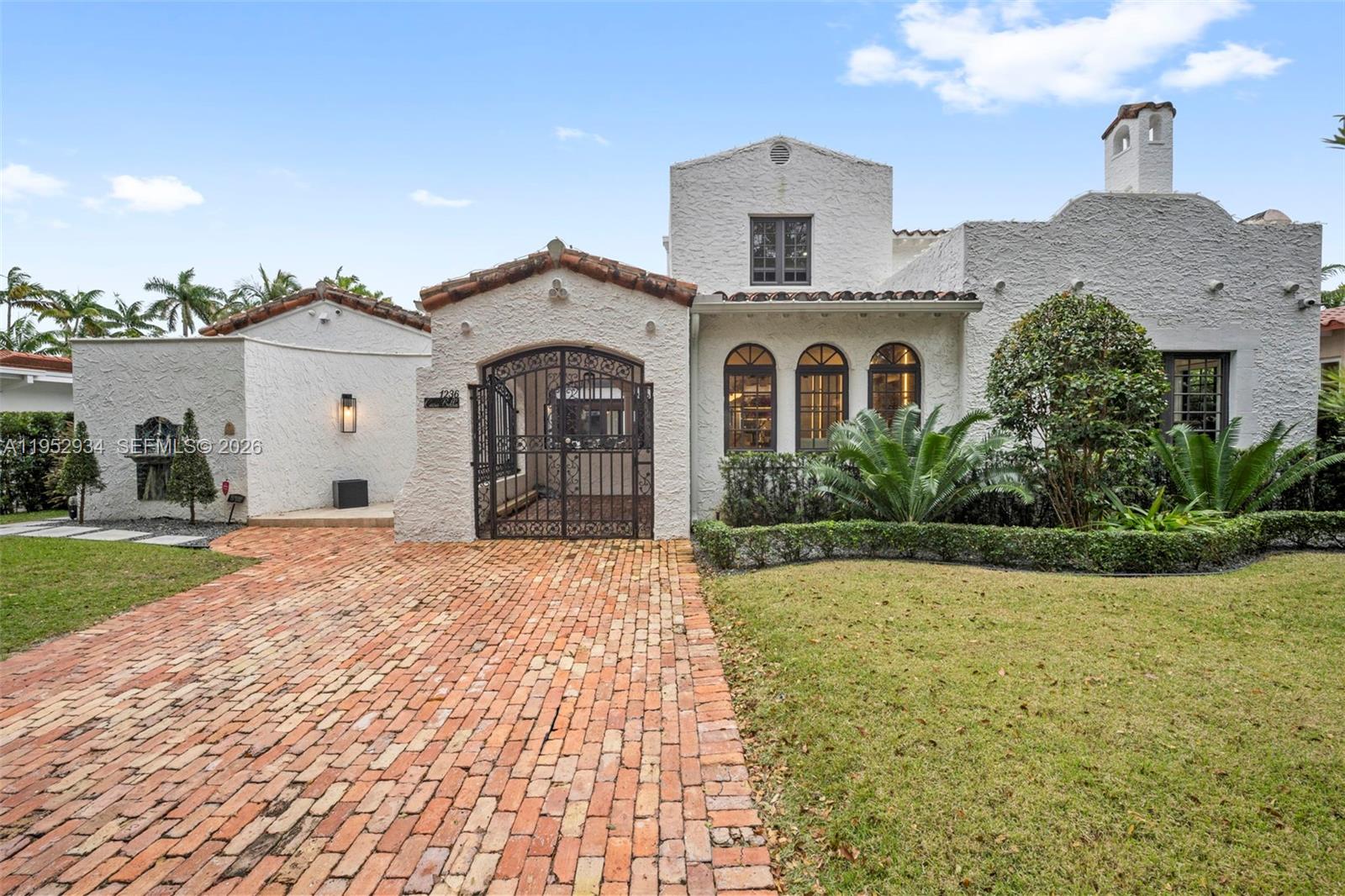 A white stucco house features a brick driveway, arched iron gate, and arched windows — 1236 Obispo Ave, Coral Gables FL 33134, CORAL GABLES, FL