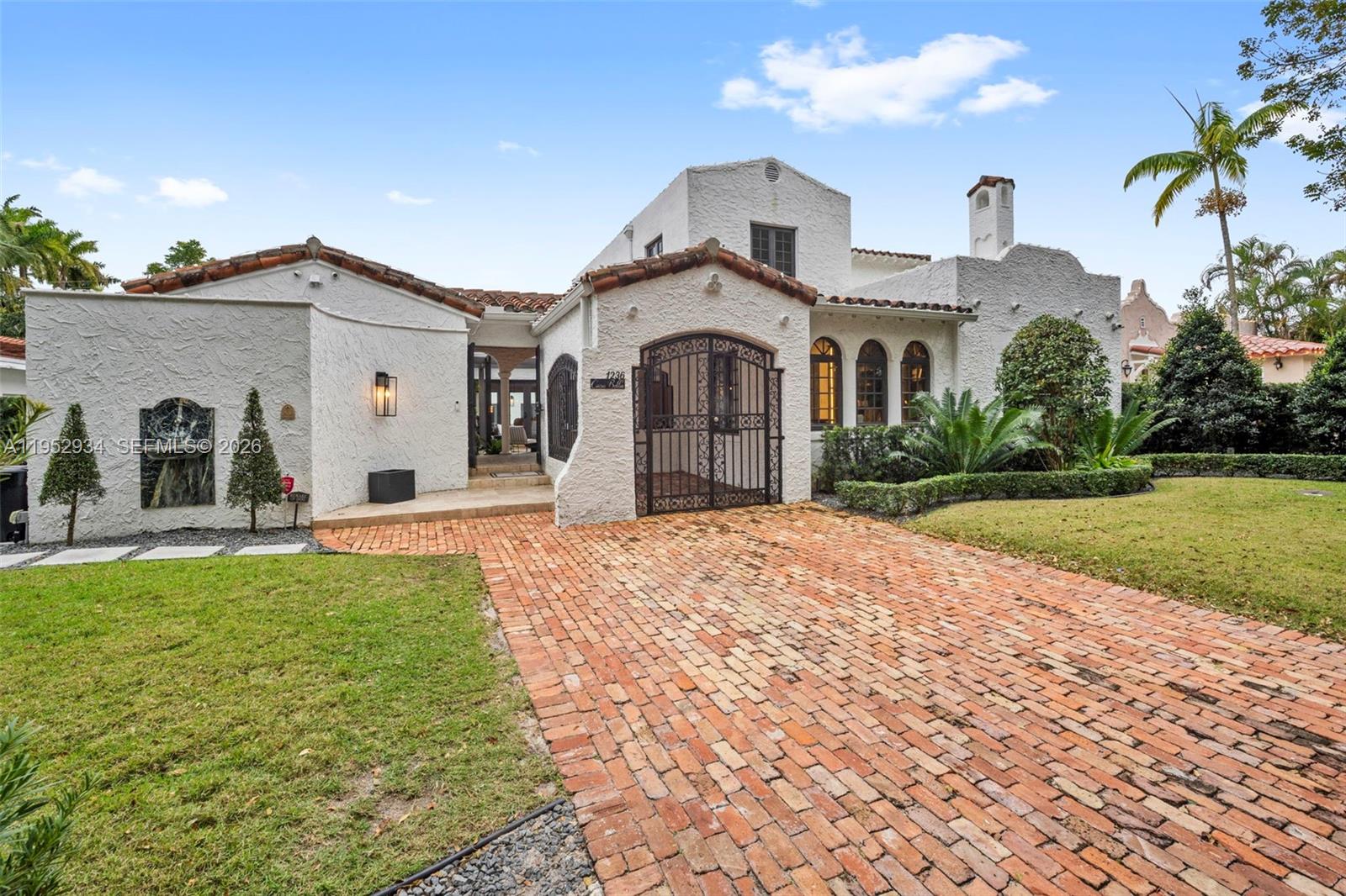 A white stucco house with a brick driveway and an arched iron gate entrance — 1236 Obispo Ave, Coral Gables FL 33134, CORAL GABLES, FL