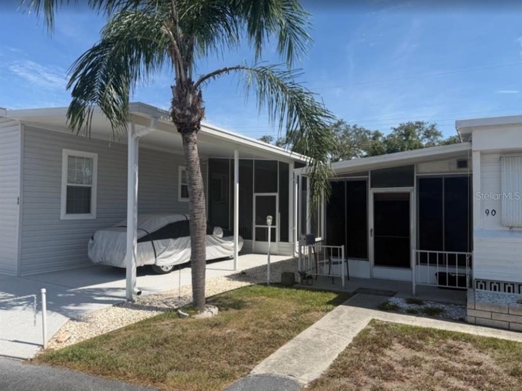 A single-story manufactured home with a carport, screened-in porch, and a palm tree in front — 90 SOUTHWINDS DRIVE, SARASOTA, FL