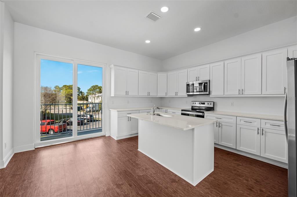 A kitchen with white cabinets, a central island, stainless steel appliances, and a sliding glass door — 5728 BISCAYNE COURT, NEW PORT RICHEY, FL