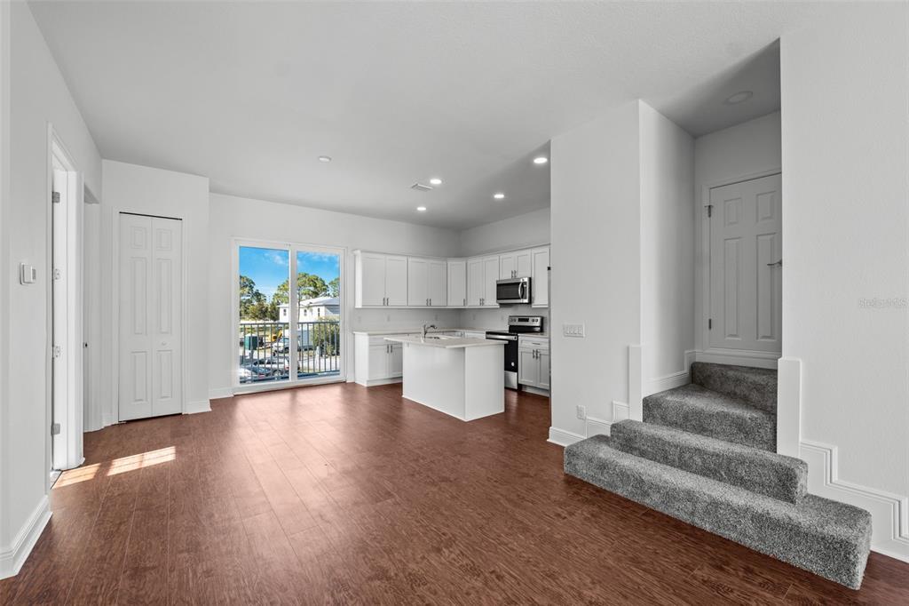 An open-concept kitchen and living area features white cabinetry, a center island, and carpeted stairs — 5728 BISCAYNE COURT, NEW PORT RICHEY, FL