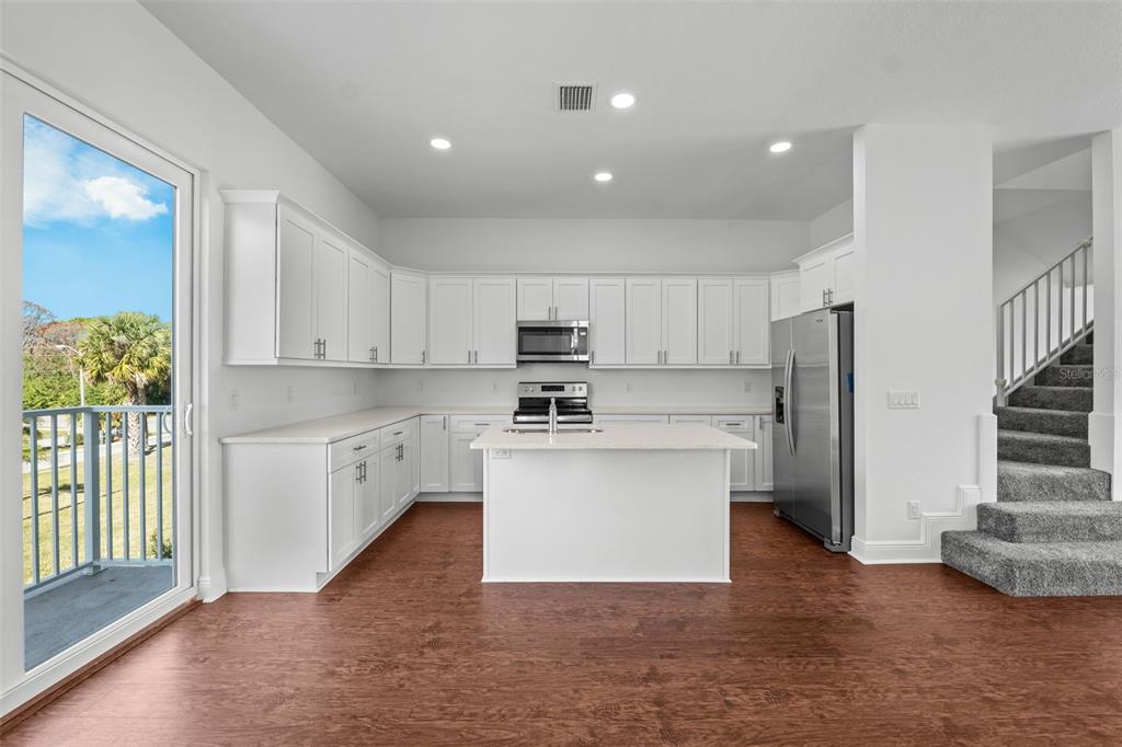 A kitchen with white cabinets, a central island, stainless steel appliances, and wood-look flooring — 5728 BISCAYNE COURT, NEW PORT RICHEY, FL
