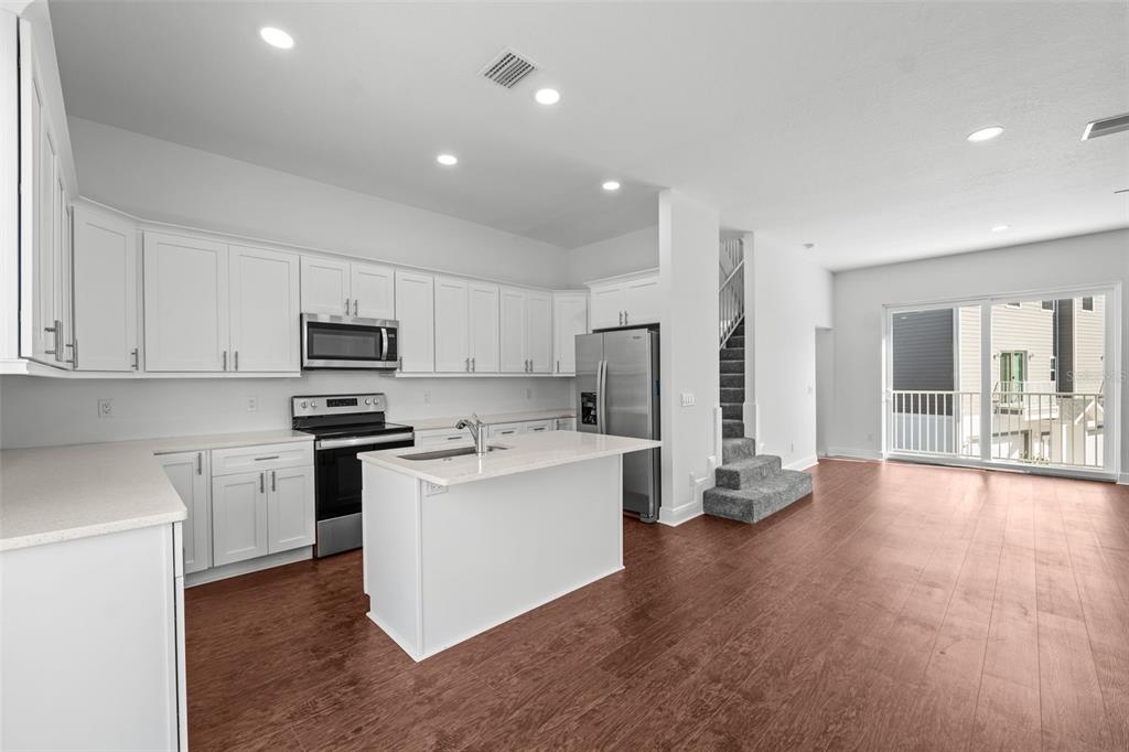 A kitchen with white cabinets, stainless steel appliances, and an island opens to a living area — 5728 BISCAYNE COURT, NEW PORT RICHEY, FL