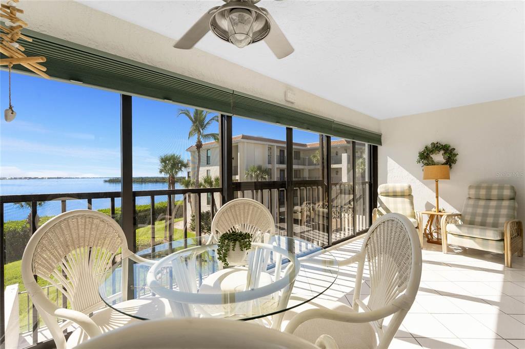 A sunroom features a glass dining table, wicker chairs, tiled floors, and a waterfront view — 1551 BEACH ROAD UNIT 306, ENGLEWOOD, FL