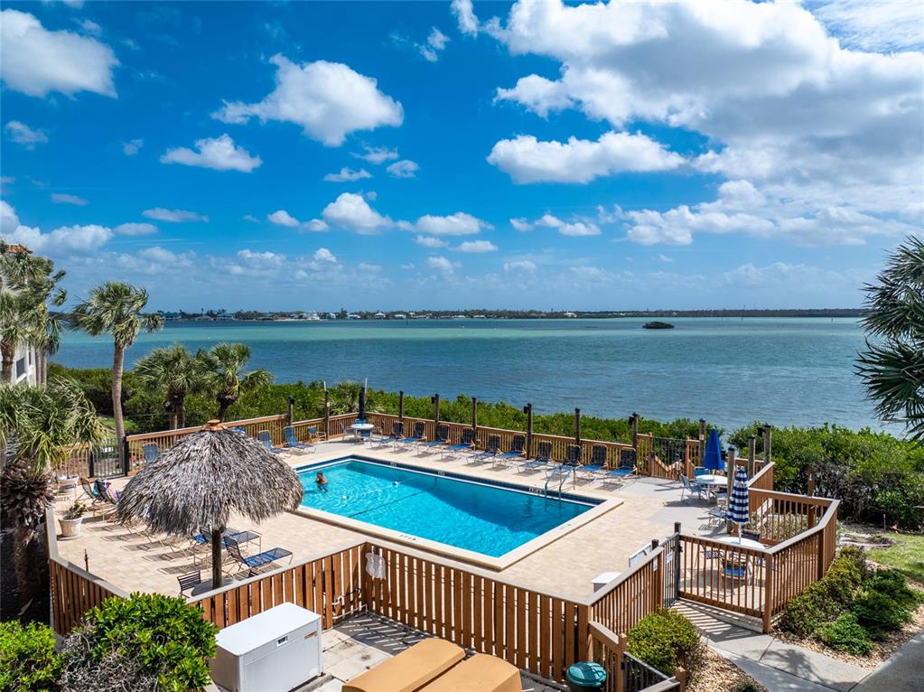 An elevated view of a swimming pool with a tiki umbrella overlooking a large bay — 1551 BEACH ROAD UNIT 306, ENGLEWOOD, FL